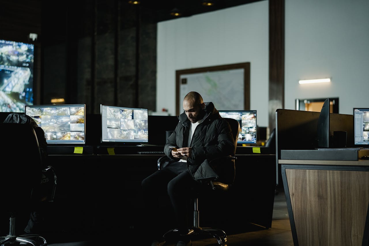digital Security officer seated in a dimly lit control room, analyzing multiple surveillance screens.