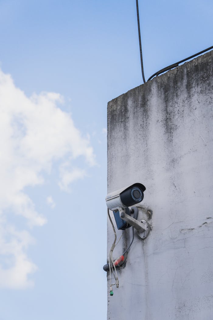 Services-01 Outdoor security camera attached to a weathered concrete wall under clear sky.